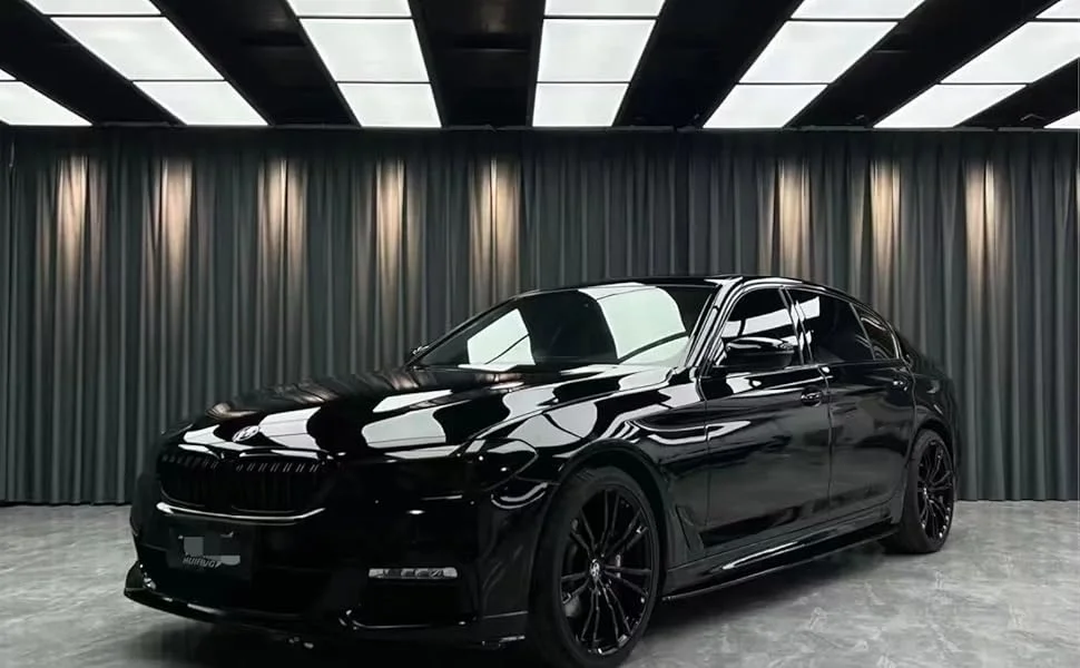 A sleek car with black gloss paint protection film (PPF) parked inside a well-lit studio, showcasing its reflective, high-gloss finish